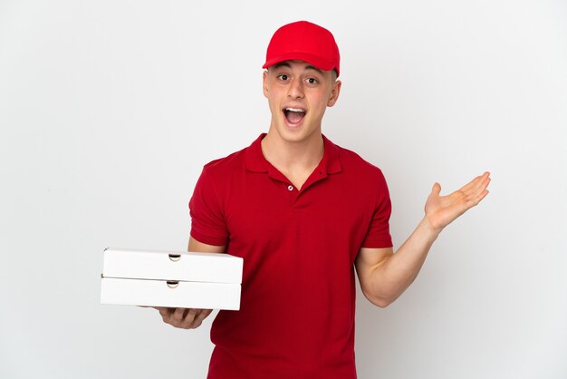 Pizza delivery man with work uniform picking up pizza boxes isolated on white with shocked facial expression