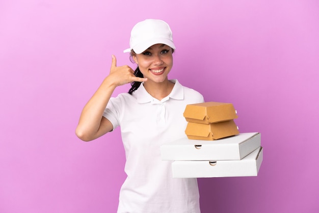 Foto consegna pizza ragazza russa con divisa da lavoro che preleva scatole per pizza e hamburger isolati su sfondo viola facendo gesto telefonico. richiamami segno