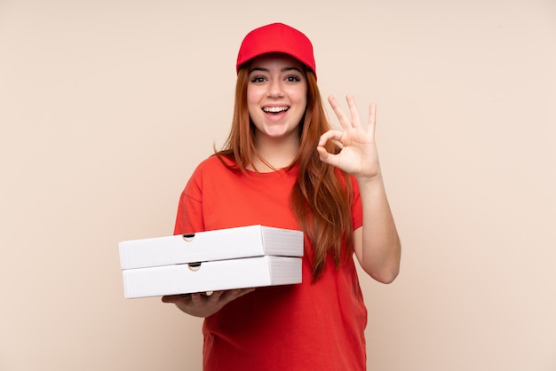 Pizza delivery teenager woman holding a pizza showing an ok sign with fingers