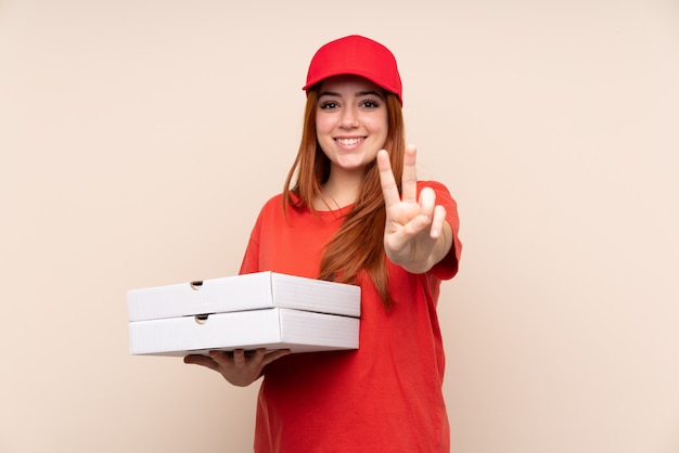 Donna dell'adolescente di consegna della pizza che tiene una pizza che sorride e che mostra il segno di vittoria