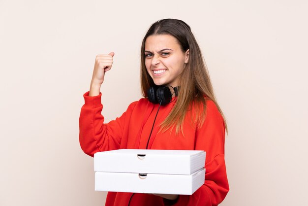 Donna di consegna della pizza che tiene una pizza sopra la parete isolata che celebra una vittoria