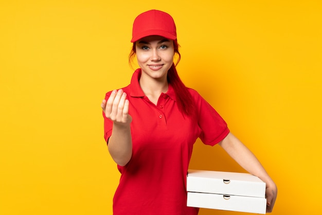 Женщина доставки пиццы держит пиццу над изолированной стеной, приглашая прийти с рукой.