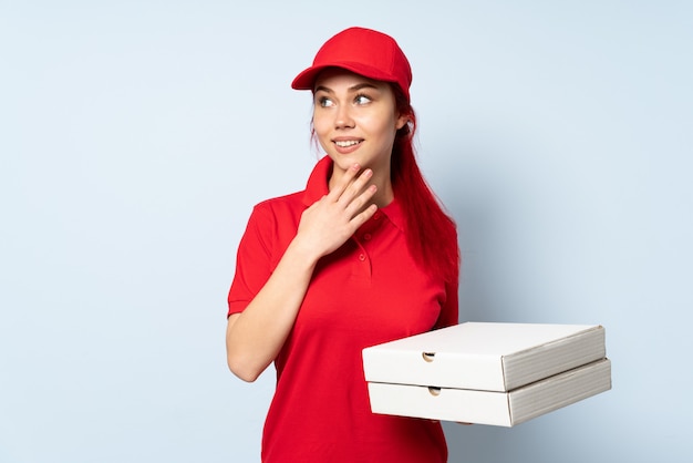 Pizza delivery woman holding a pizza over isolated wall looking up while smiling