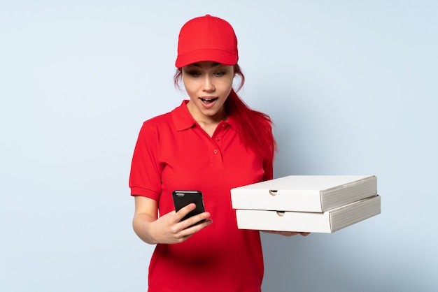 Pizza delivery woman holding a pizza over isolated wall surprised and sending a message