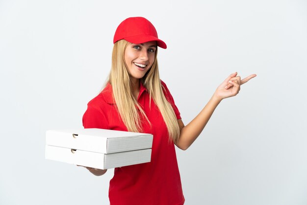 Pizza delivery woman holding a pizza isolated on white wall pointing finger to the side