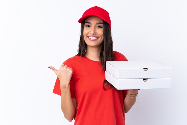 Pizza delivery woman holding a pizza over isolated white wall pointing to the side to present a product