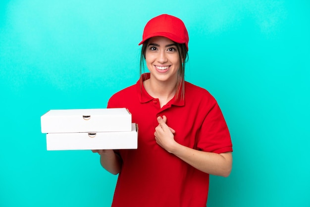작업복을 입은 피자 배달 여성이 놀란 표정으로 파란색 배경에 격리된 피자 상자를 집어들다