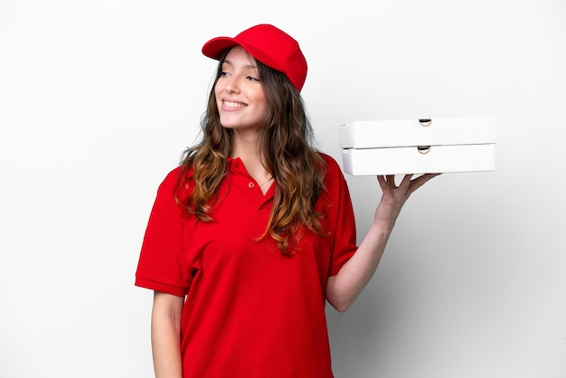 Donna di consegna della pizza con uniforme da lavoro che raccoglie scatole di pizza isolate su sfondo bianco che guarda di lato e sorride