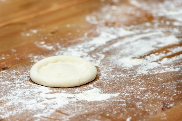 Photo pizza dough basis for baking pizza on a wooden table closeup