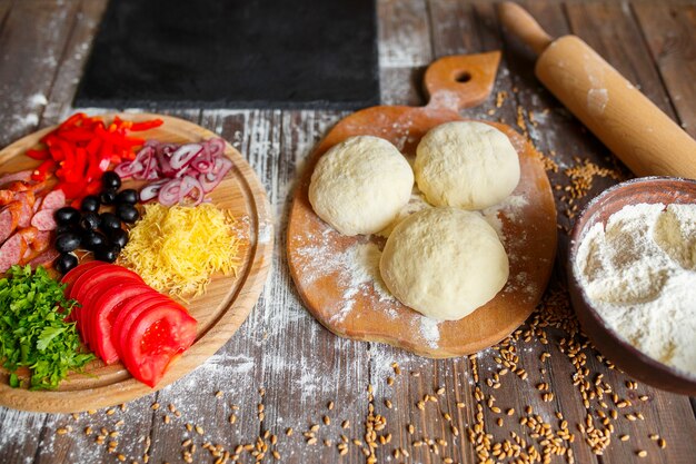 Pizza dough with ingredients on wood table