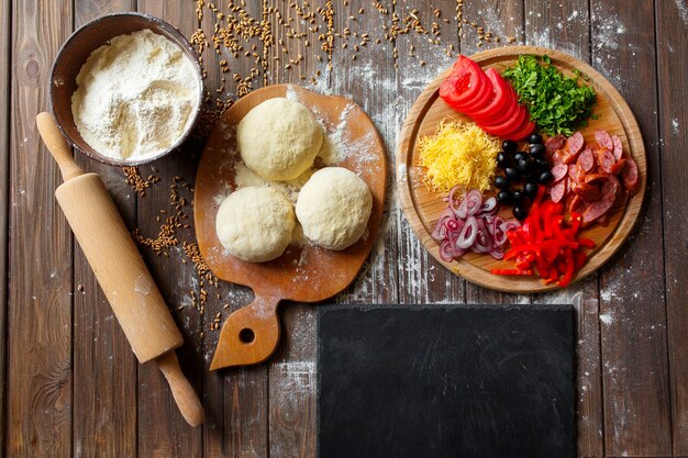 Pizza dough with ingredients on wood table