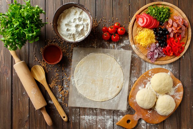 Pizza dough with ingredients on wood