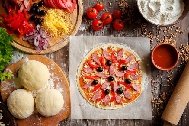 Pizza dough with ingredients on wood