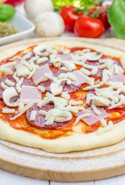 Pizza dough with tomato sauce, salami, bacon, mushrooms and cheese
