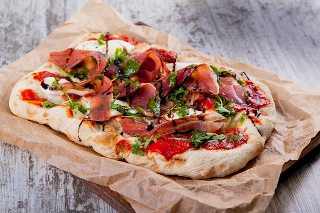 Pizza on fluffy dough with Parma ham pear cheese and curd cheese and balsamic sauce with rucola