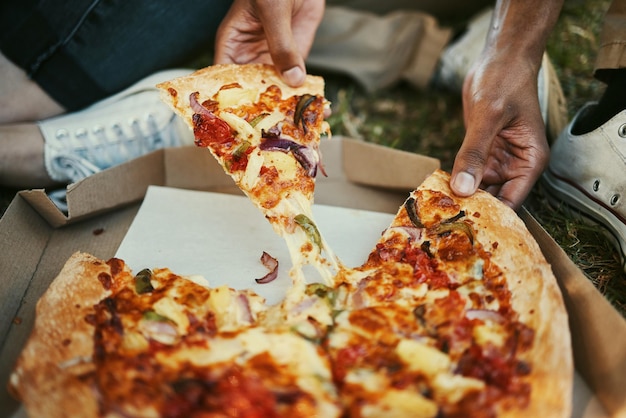 Pizza food and hands of a couple eating in a park picnic and relax on an outdoor date together Hungry fast food and zoom of man and woman with lunch or dinner in nature for peace and calm