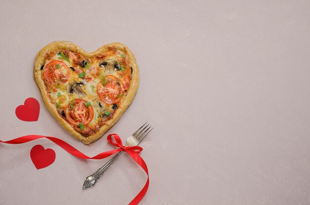 Pizza in de vorm van een hart op een beige tafel met rode harten met een vork met een rood lint. Bestel pizza voor een romantisch diner op Valentijnsdag. Liefde.