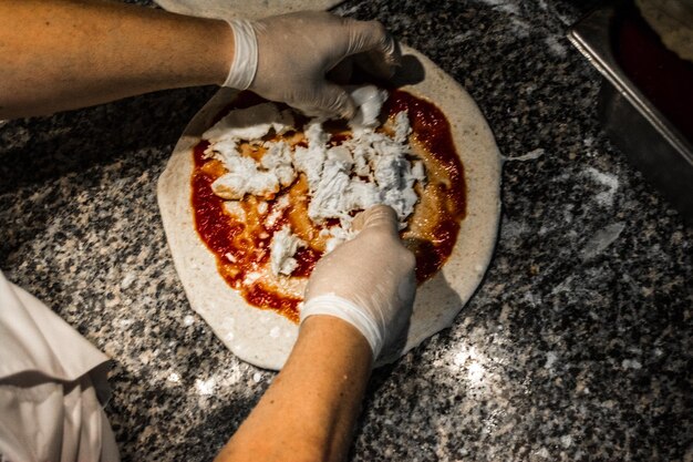 Foto pizza maken met saus en chef met handschoenen.