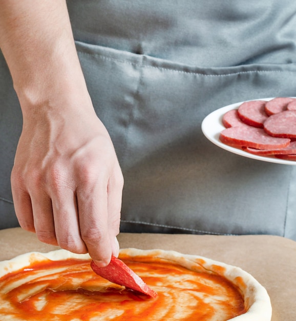 Pizza maker puts the ingredients on the dough