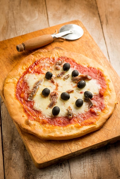 Пицца маргарита с анчоусами и маслинами на деревянной разделочной доске