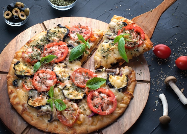 pizza met aubergine, olijven en champignons op ronde snijplank op zwarte achtergrond