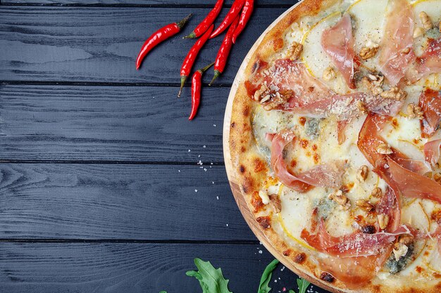 Pizza met jamon, gorgonzola en parmezaanse kaas, noten en peer. bovenaanzicht. verse zelfgemaakte italiaanse pizza. voedsel achtergrond. pizza met vlees en kaas op donkere houten achtergrond