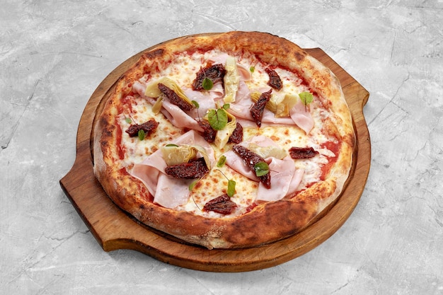 Pizza met kalfsham-kaas en zongedroogde tomaatjes op een grijze tafel