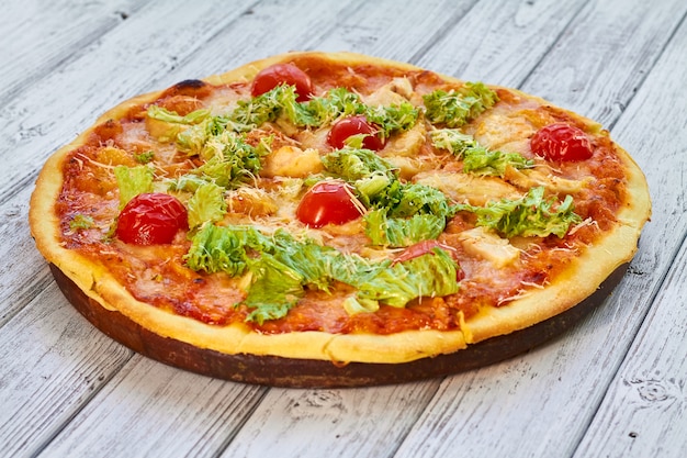 Pizza met kip, tomaten en kaas op houten tafel