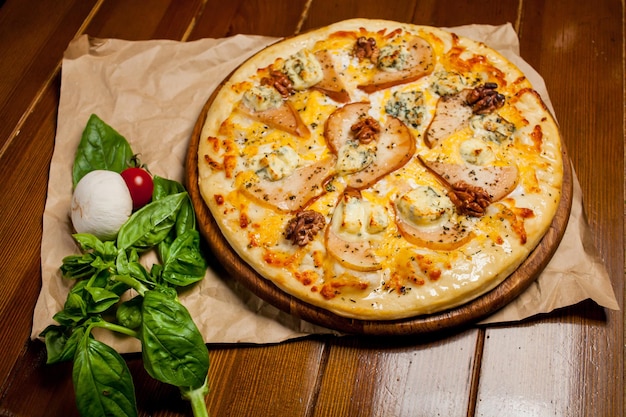 Pizza met peer, walnoten, Dorbl kaas en citroenolie. Zelfgemaakte pizza met peer, walnoten en gorgonzola op een bruin houten tafel - ambachtelijk papier. Naast de pizza ligt een champignon, zuring en cherrytomaat.