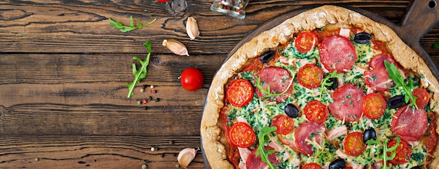 Pizza met salami, tomaten, olijven en kaas op een deeg met volkoren meel. Italiaans eten. Bovenaanzicht Plat leggen.
