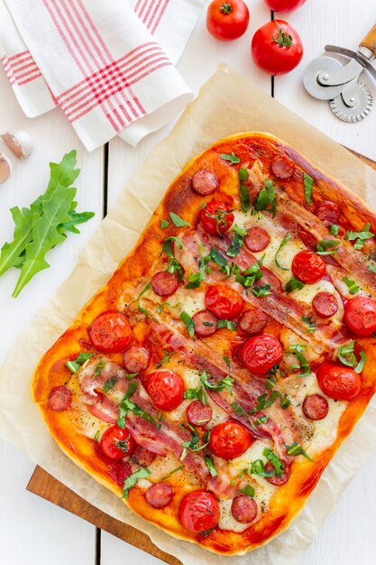 Pizza met spek, worst, mozzarella, tomaten en basilicum. Italiaanse keuken. Recept.