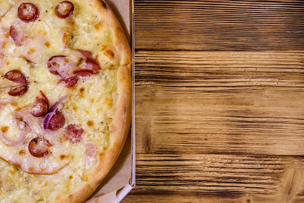 Pizza met worst, ham en Parmezaanse kaas in kartonnen doos op een houten tafel. Bovenaanzicht