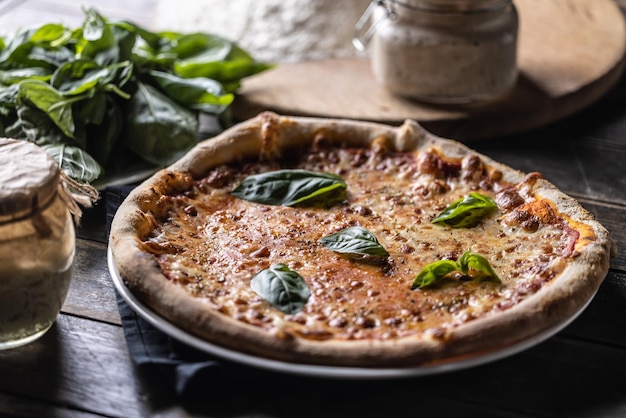 Pizza Napoli met tomatensaus mozzarella en verse basilicum op de achtergrond bloem en een potje roggezuurdesem