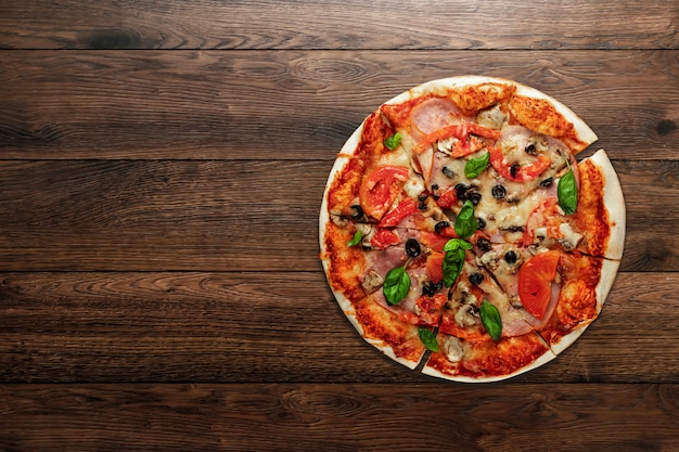 Pizza op houten met ham, olijven, tomaten en groene basilicum