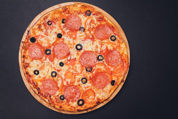 Pizza ai peperoni, mozzarella, origano su uno sfondo nero.