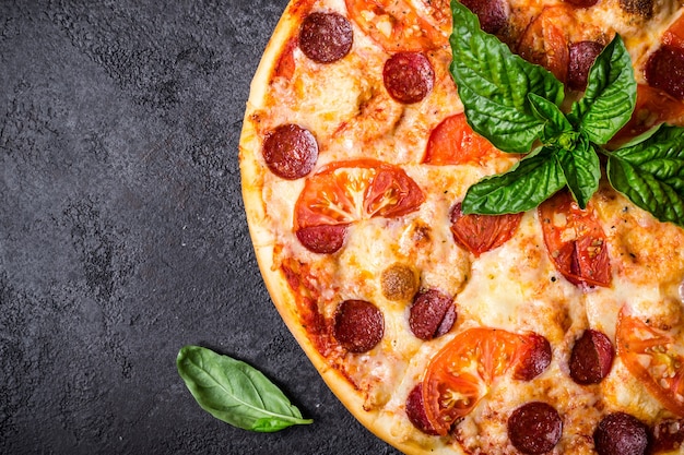 Pizza pereroni and basil on black background closeup.