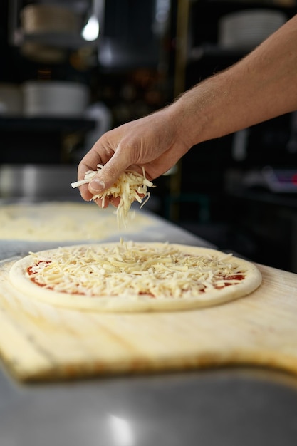 Pizza preparation process with closeup chef hands sprinkling cheese