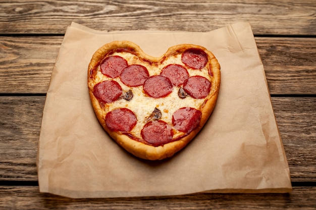 Photo pizza in the shape of a heart on a wooden table