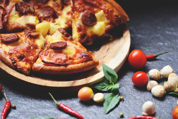 Pizza slice on wooden tray and tomato chilli basil leaf on dark