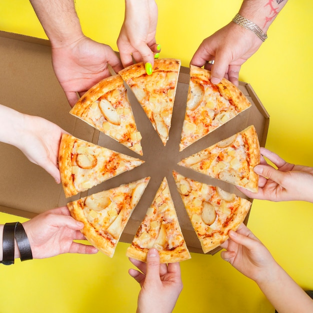 Pizza slices in the hands of a group of people top view on a yellow space. Concept photo for pizzerias.