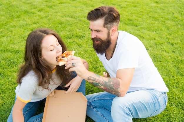 Pizza time summer picnic on green grass family weekend couple in love dating fast food bearded man hipster and adorable girl eat pizza happy couple eating pizza feeding his girlfriend