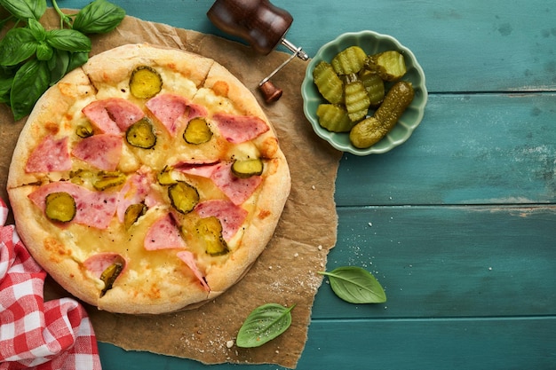 Foto pizza traditioneel bacon pizza met ham paddenstoelen ingelegde komkommer en kaas en kookingrediënten tomaten basilicum op houten tafel achtergrond italiaans traditioneel eten top view mock up