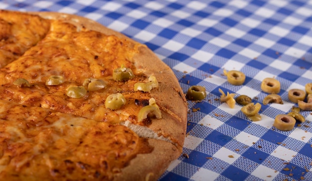 Треугольник пиццы с желтым сыром и оливками на голубой скатерти