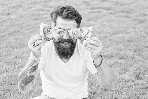 Foto pizza weekend fastfood bebaarde man hipster eet pizza gelukkige man student die pizza eet plezier diëten zal wachten zomer picknick op groen gras hipster heeft pizzaglazen