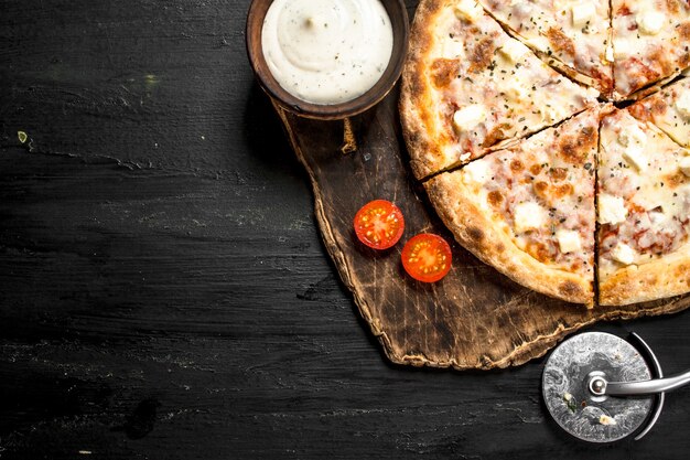 Pizza with cheese and aromatic herbs on black chalkboard.