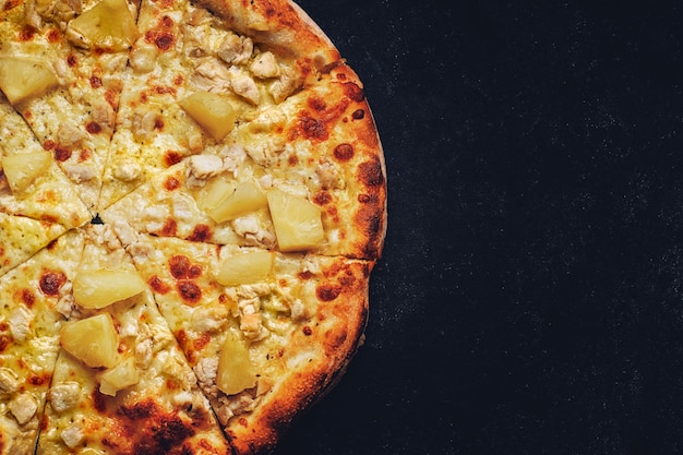 Pizza con formaggio, ananas e pollo su fondo scuro