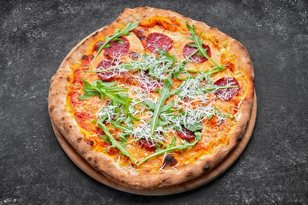 Pizza con formaggio, salsiccia e rucola, su una tavola di legno, su uno sfondo scuro