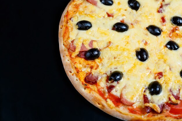 Pizza with cheese tomato sauce, olives, fresh mozzarella, parmesan and basil and meat on a dark background