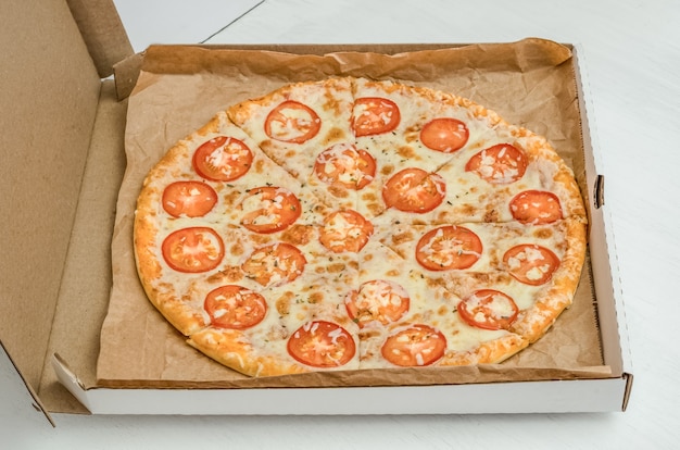 Pizza with cheese and tomatoes on a white wooden background close-up.