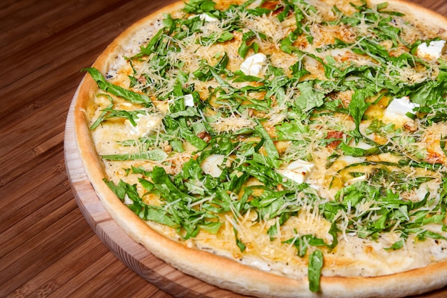 Pizza with cheeses and herbs on a wooden plate. Close-up, selective focus